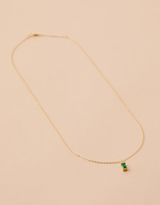 Gold necklace with a green gemstone on a beige background