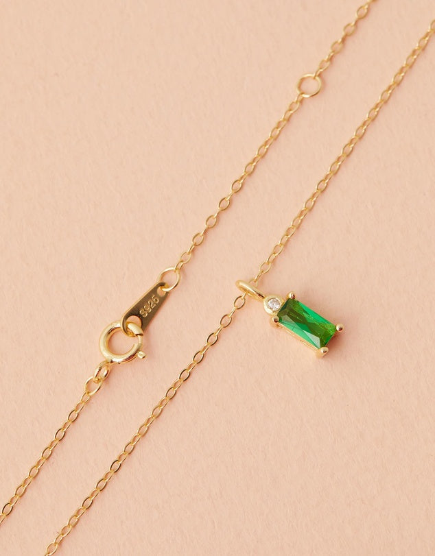 Gold necklace with a green gemstone pendant on a beige background