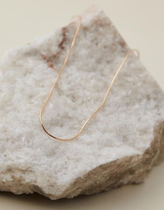 Snake Chain gold laid out on a beige stone