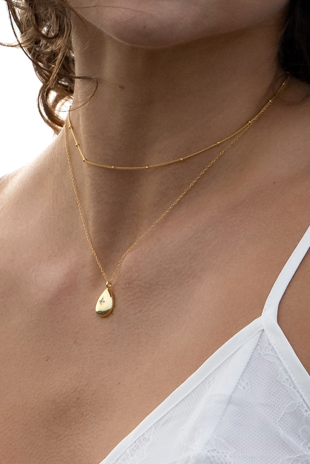 Close-up of a person wearing a gold necklace with a teardrop pendant and the Gold Dot Chain