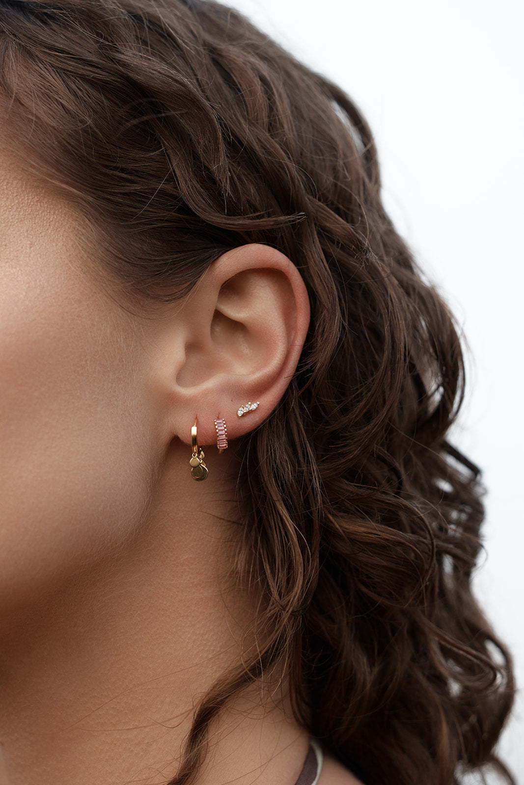 Close-up of an ear wearing Lennox Huggies - Gold & Pink and other multiple earrings