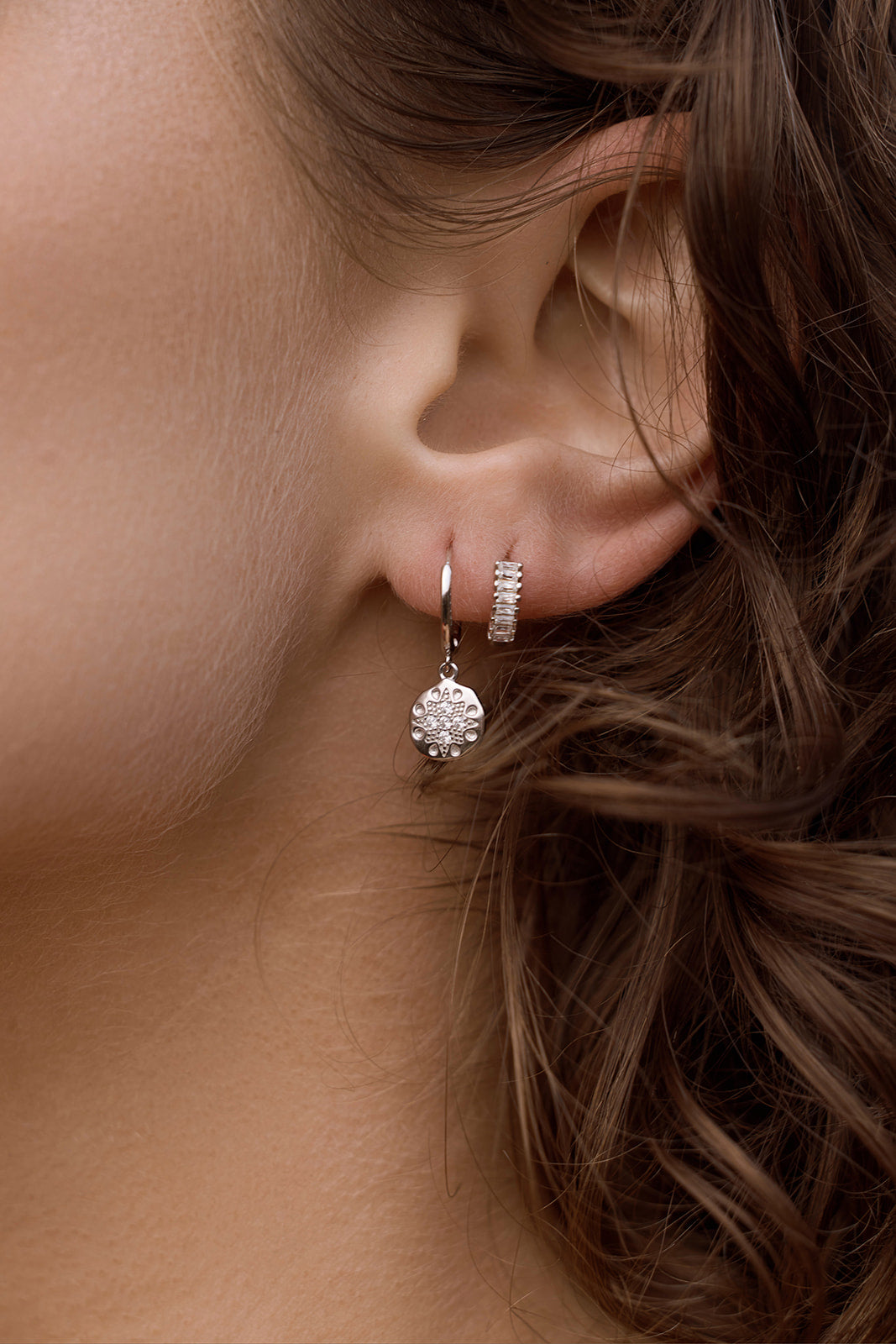 Close-up of a person wearing Lennox Huggies - Silver earrings with a blurred background