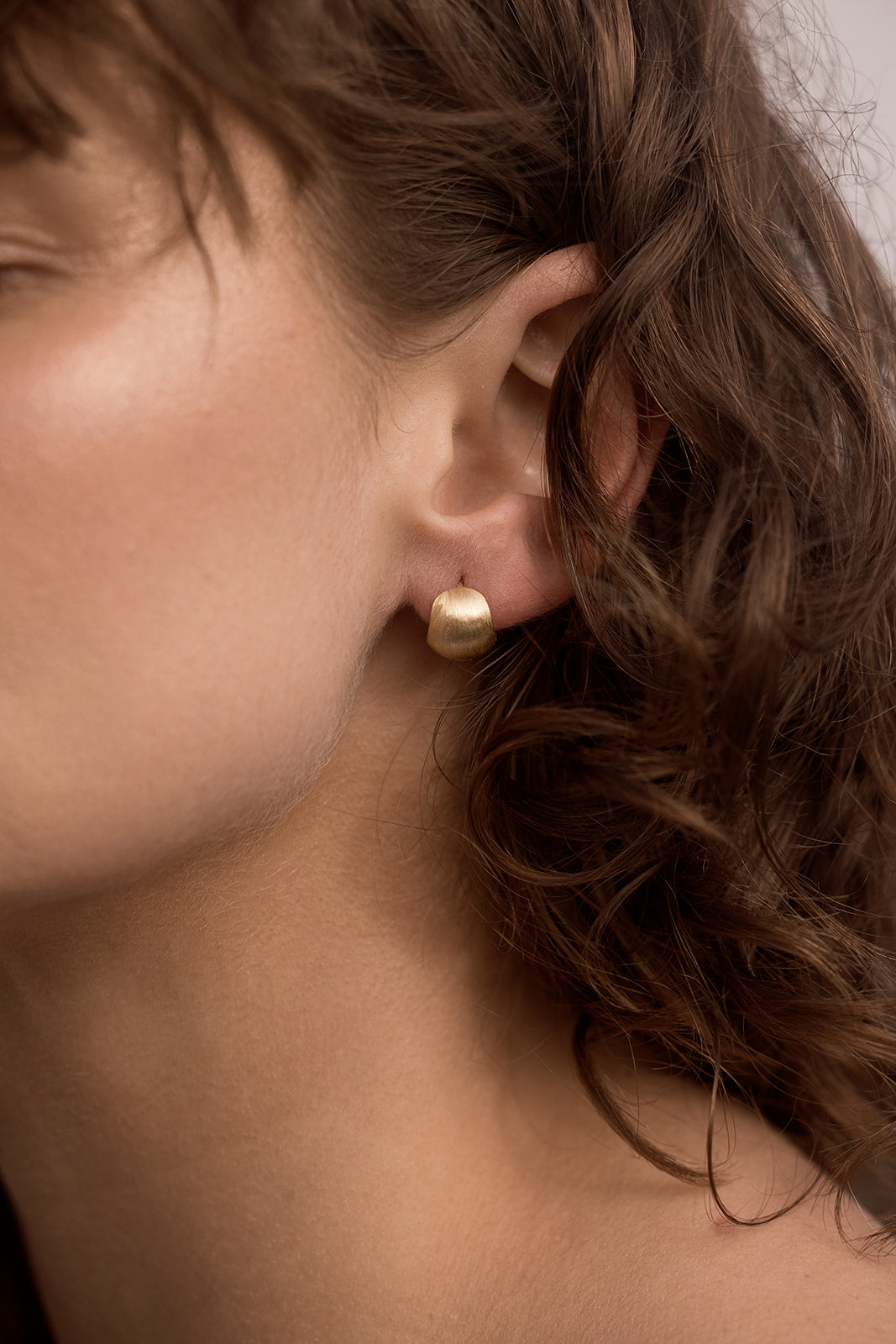 Milano Hoop Earrings Close-up of a person wearing a gold earring with soft focus on hair and skin.