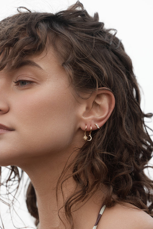 Close-up of a woman wearing gold hoop earrings with a star and a moon Night Sky Huggies - Gold