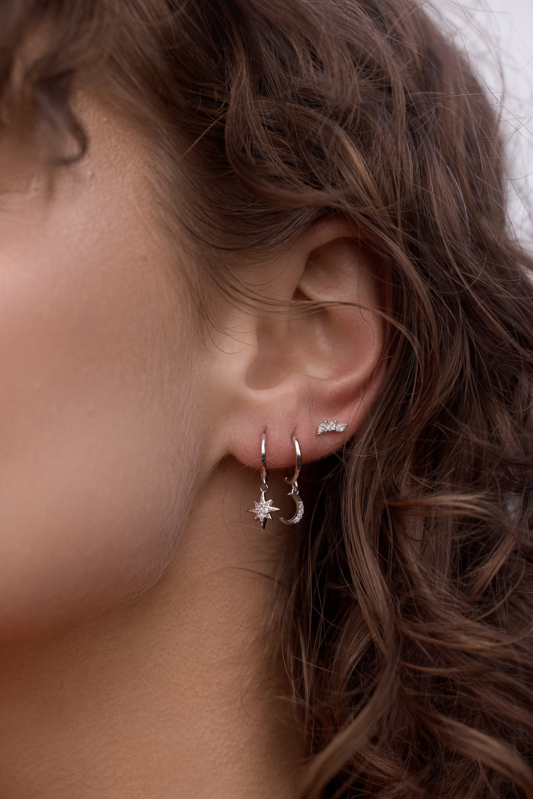 Night Sky Huggies - Silver Close-up of a person wearing silver hoop earrings with star and moon designs.