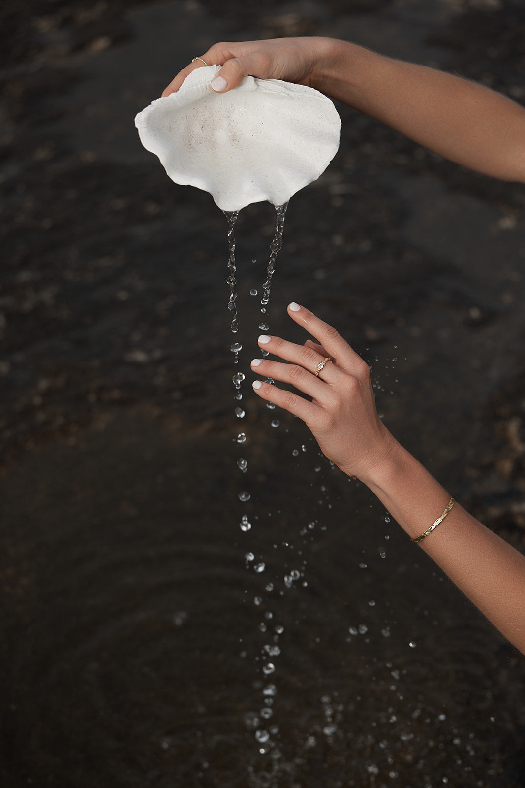 Person holding a white shell over water, with water dripping from it and wearing Remi Cuff bangle