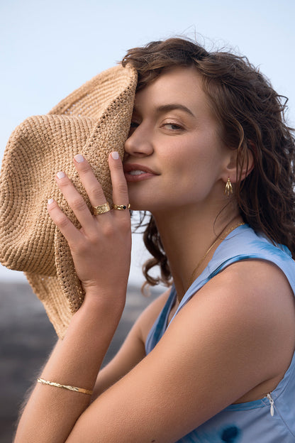 Woman holding a straw hat against her face wearing the Remi Cuff bangle
