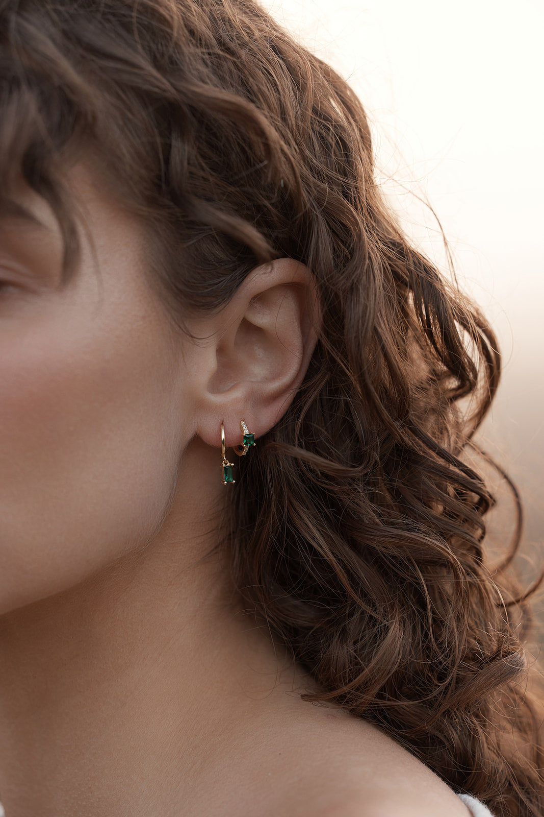 Close-up of a person wearing Rita Huggies - Emerald & Gold earrings