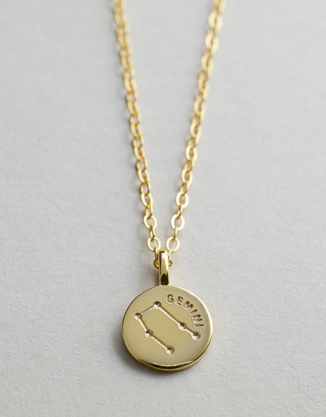 Gold Starsign_Necklace with a round pendant featuring the Gemini zodiac sign on a light gray background