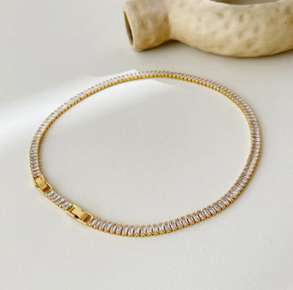 Tennis necklace with embellished detailing, displayed on a white surface.