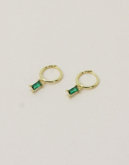 Gold hoop earrings with green gemstones on a light gray background