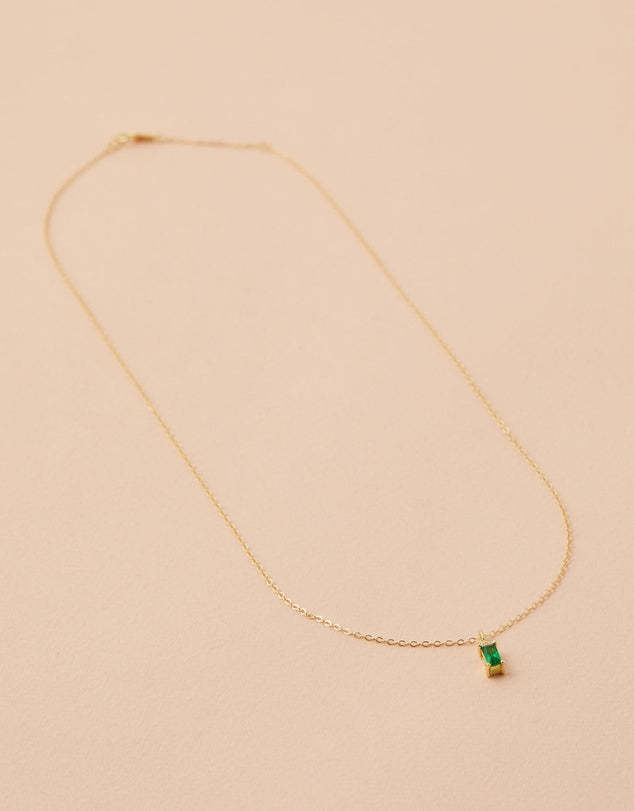 Gold necklace with a green gemstone on a beige background