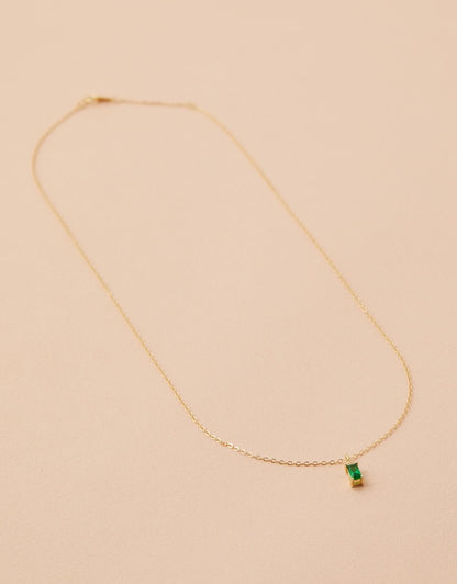 Gold necklace with a green gemstone on a beige background