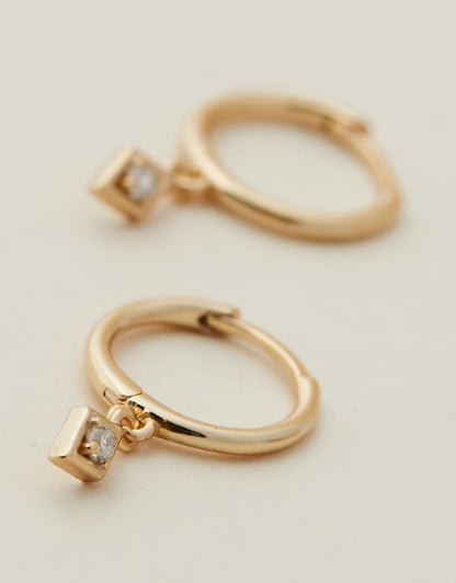 Ava Diamond Huggies - Gold earrings close up on beige back ground