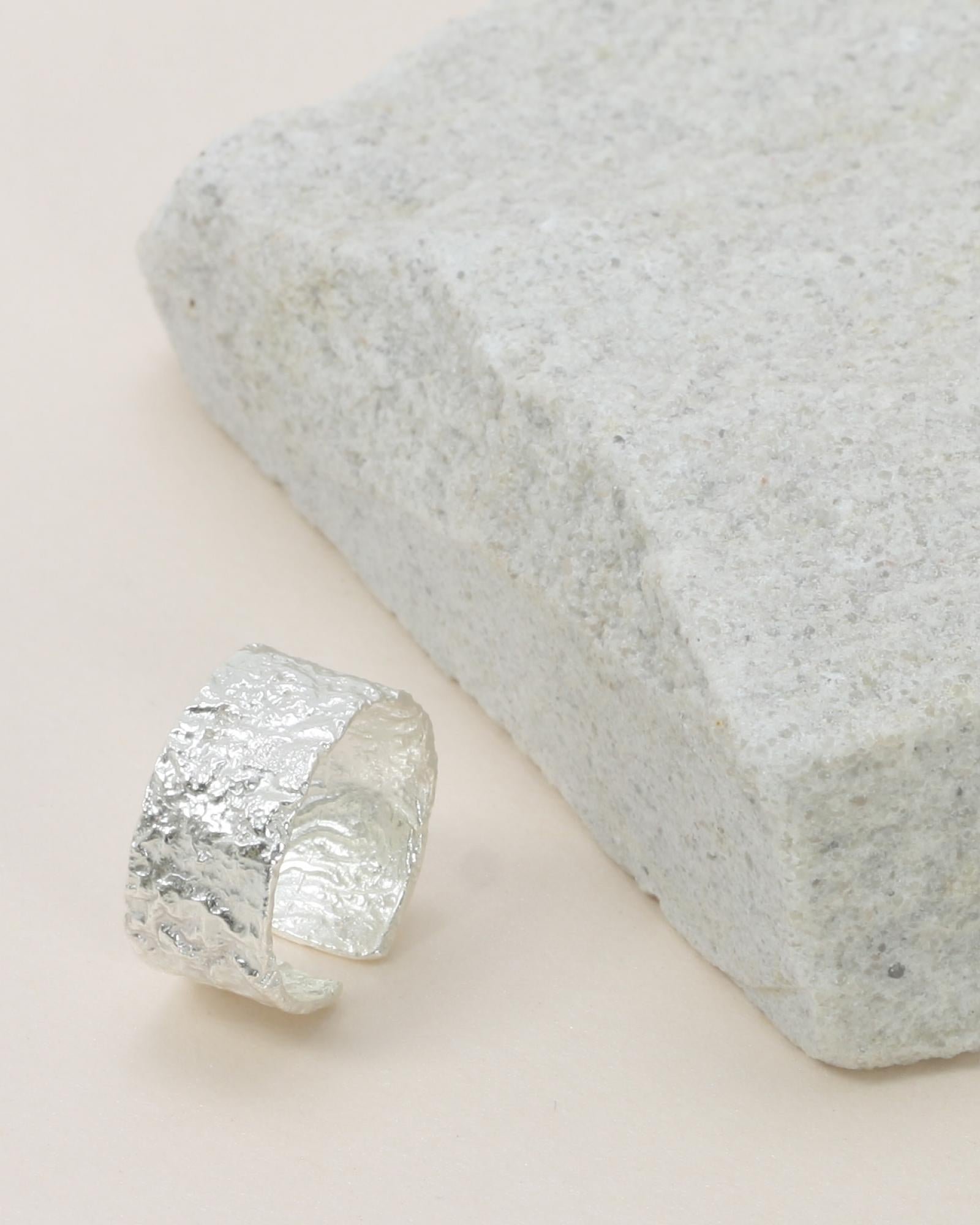 A Noah Textured Ring - Silver silver-colored cuff ring with foiling details, displayed on a textured surface.