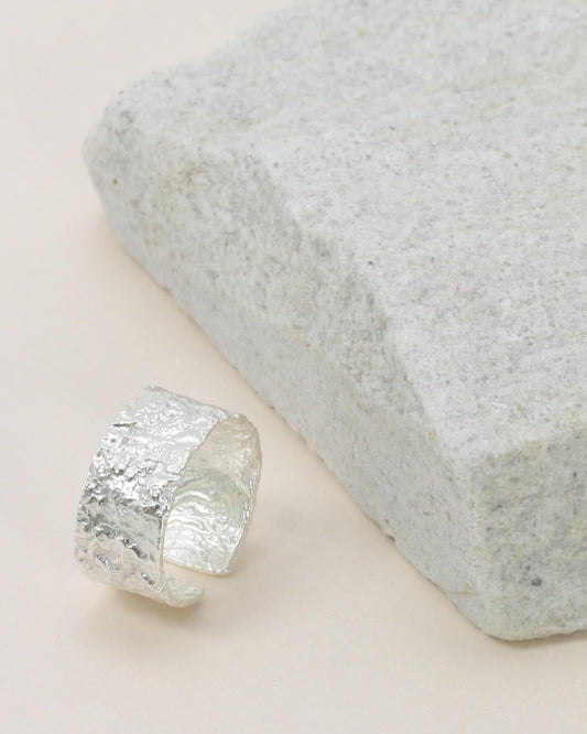 A Noah Textured Ring - Silver silver-colored cuff ring with foiling details, displayed on a textured surface.