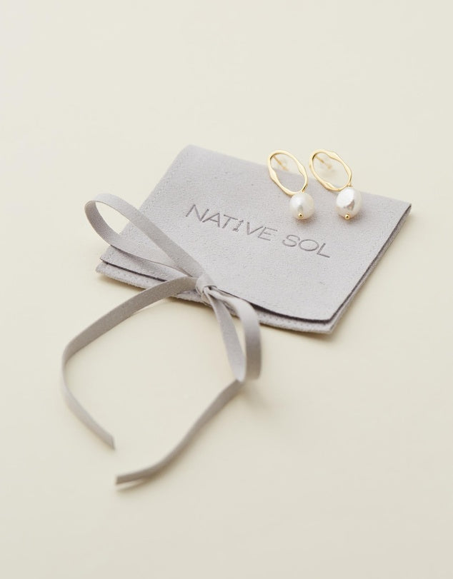 Nola Drop Pearl Earrings laid out on grey branded jewellery pouch