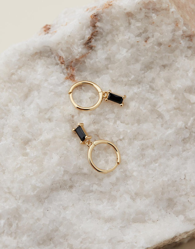 Rita Huggies - Black & Gold earrings laid out on a beige stone