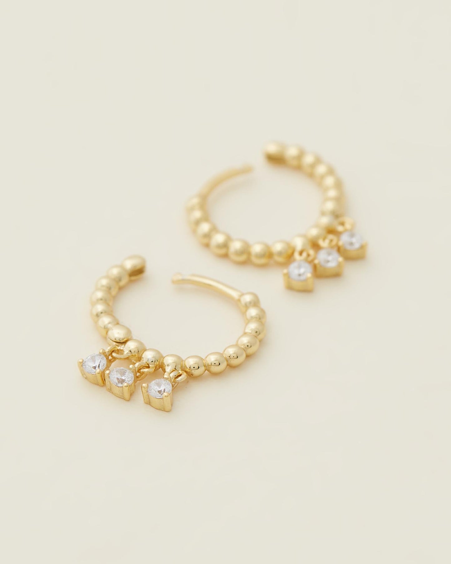 Sage Huggies - Gold close up of earrings on beige background